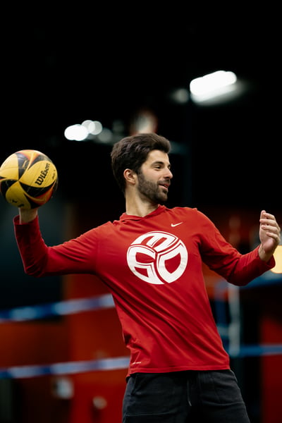 A player in red holds a ball with his right arm extended.