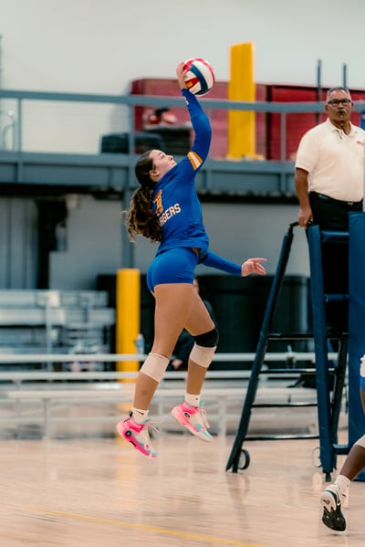 A player in blue reaches overhead for the ball.