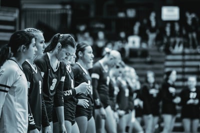 Players in black jerseys with white numbers 3, 2, and 4 stand on the court. A player in a white jersey is on the left.