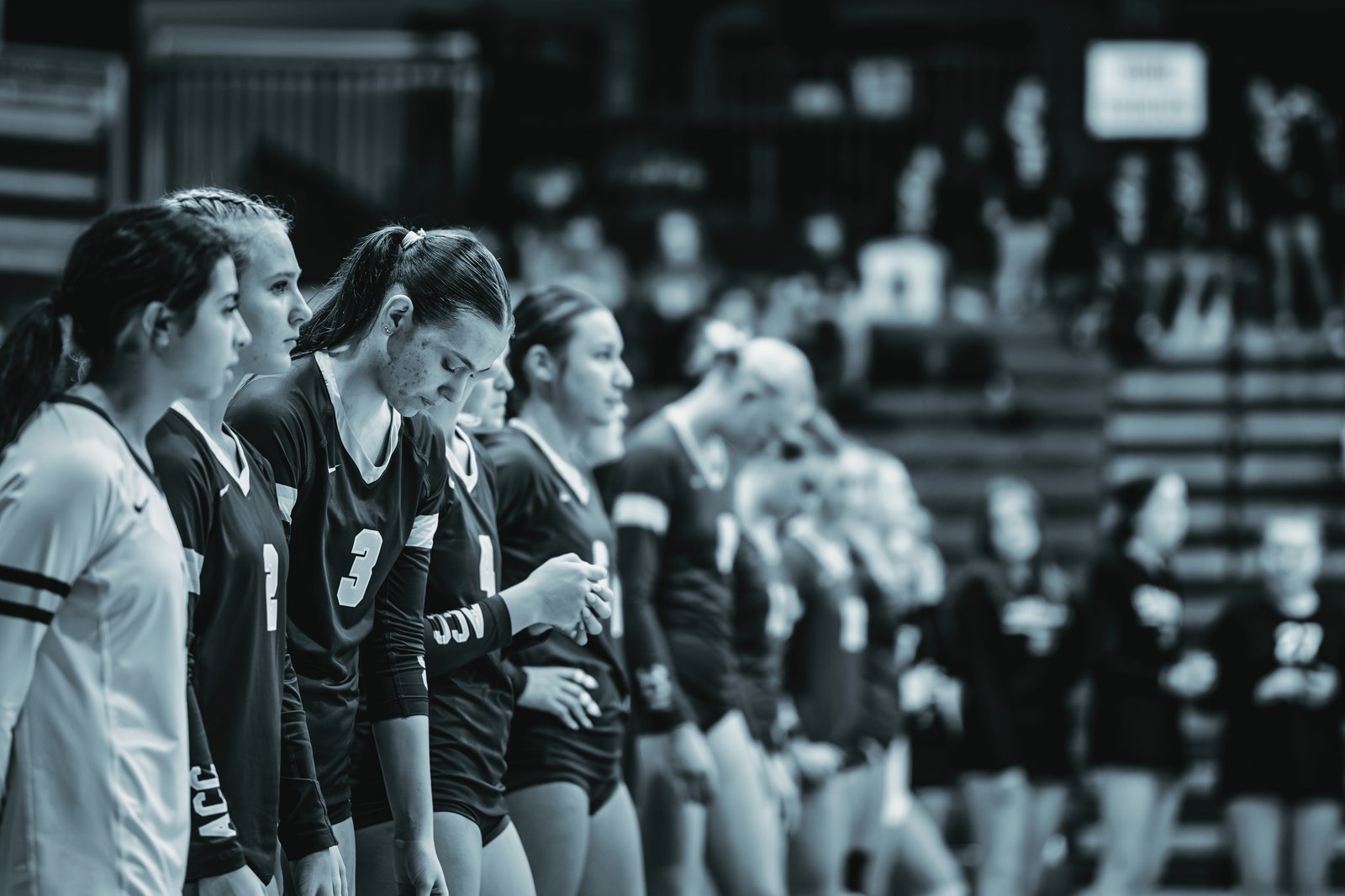 Players in black jerseys with white numbers 3, 2, and 4 stand on the court. A player in a white jersey is on the left.