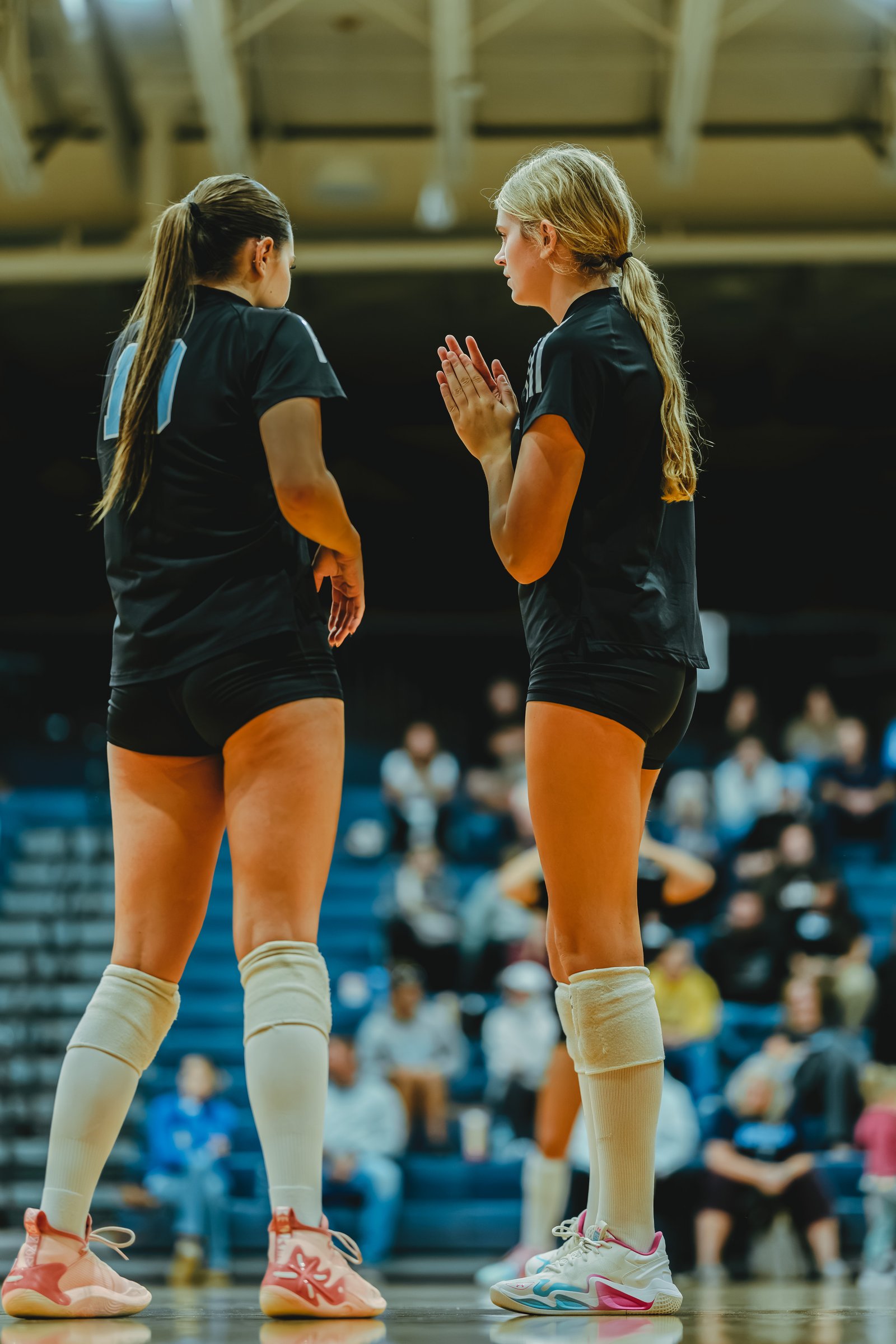 Two players in black jerseys, one with number 11, stand on the court during a volleyball game.