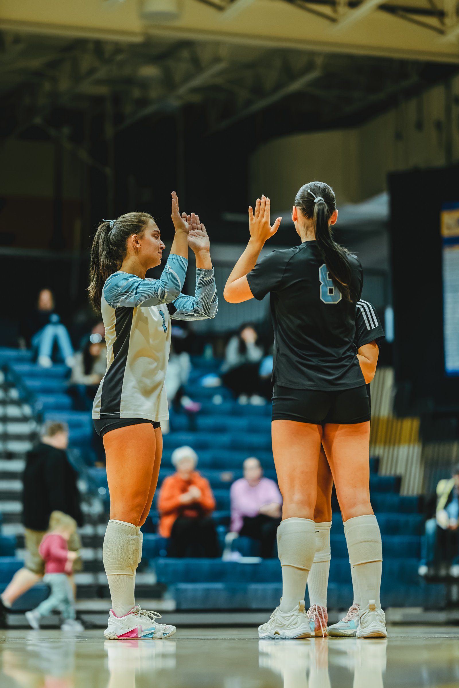 A player in a white and blue jersey with number 1 high-fives a player in a black jersey with number 6 during a volleyball game.