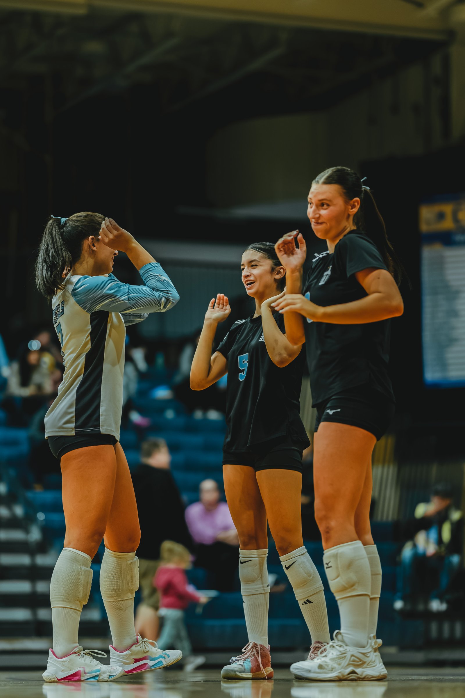 Three players celebrate on the court. Player 5 in black and player 10 in black are visible, along with a player in a light blue and white jersey.