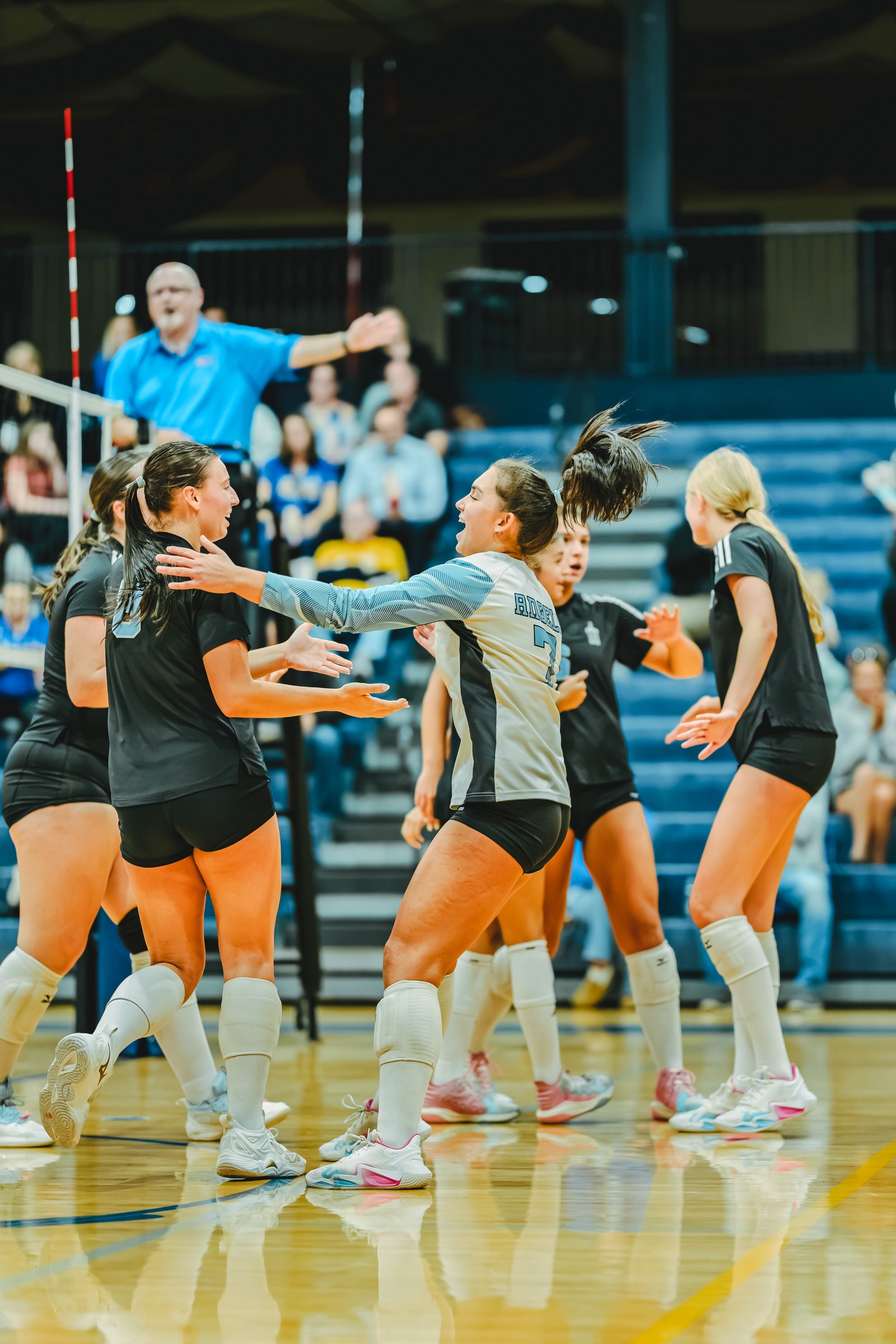 Players in black and white jerseys celebrate on the court. Player 7 in white and black has a ponytail. Player 3 in black has a ponytail.