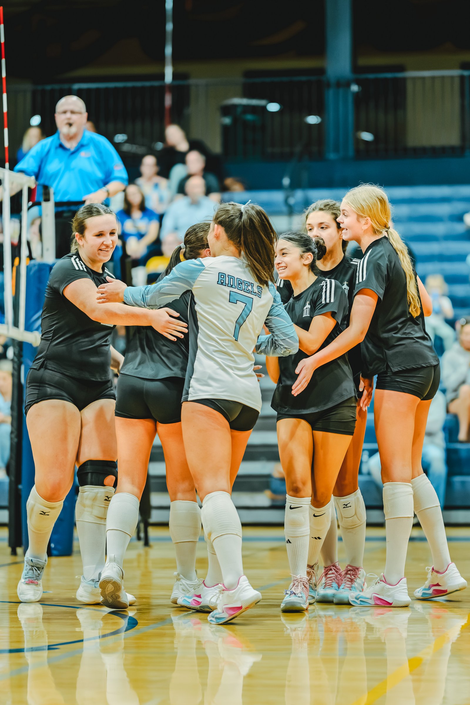 Players in black and white jerseys celebrate on the court. Player 7 wears a white jersey with blue lettering. Other players wear black jerseys.