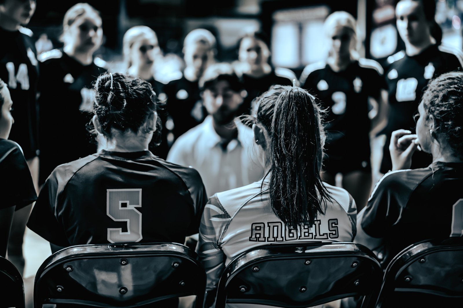 Players in black and white jerseys sit on a bench, with one player wearing number 5 and another with "ANGELS" on their jersey.