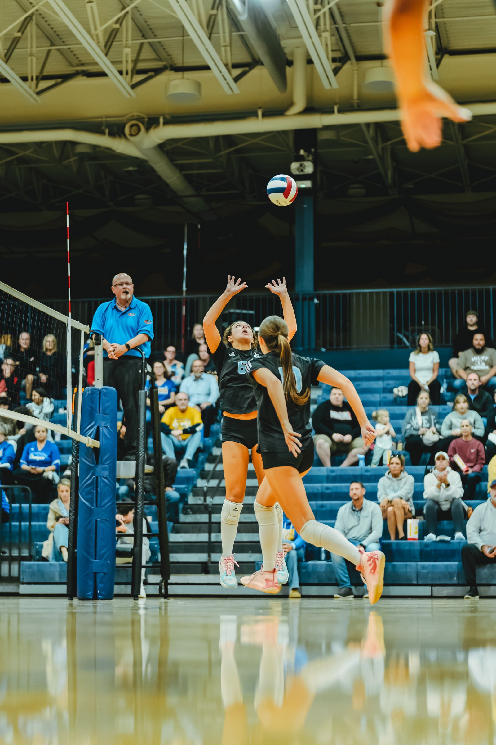 A player in black with jersey number 6 jumps to hit the ball, with a player in black and jersey number 1 in front of her, during a volleyball game.