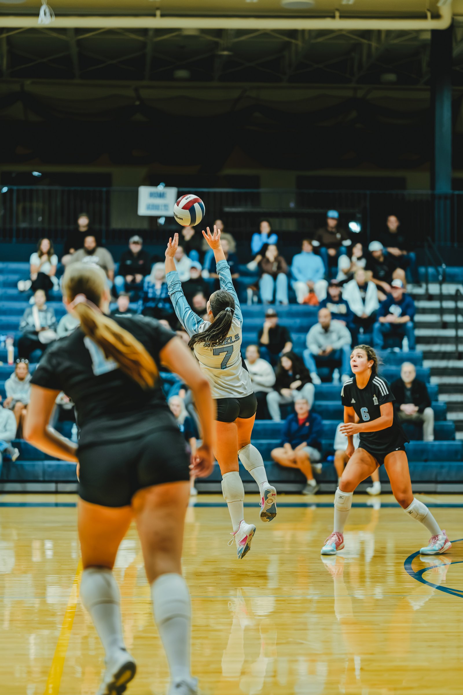 Player 7 in light blue sets the ball, with players 6 and 1 in black on the court.