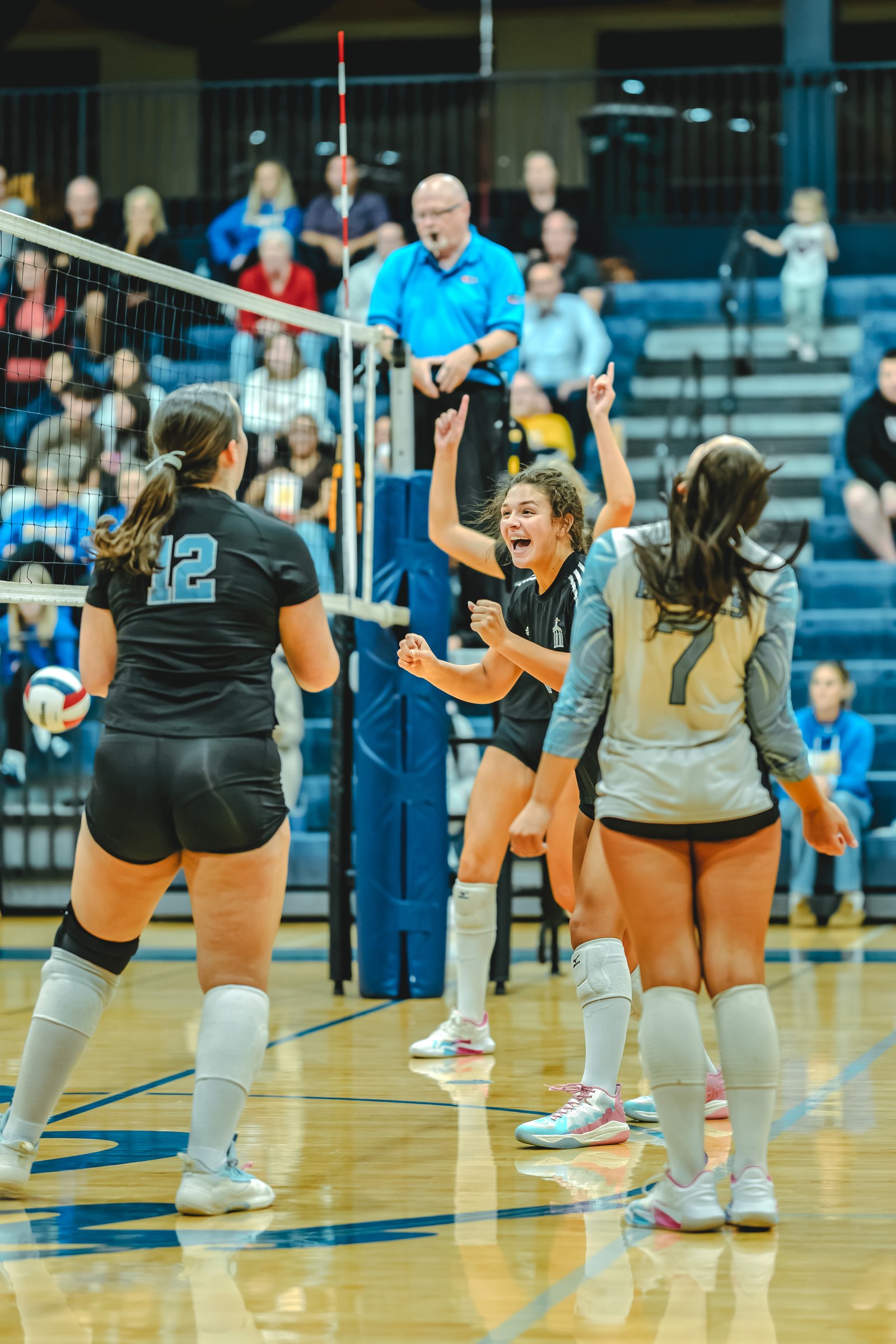 A player in black with jersey number 12 and a player in black with jersey number 7 celebrate during a volleyball game.