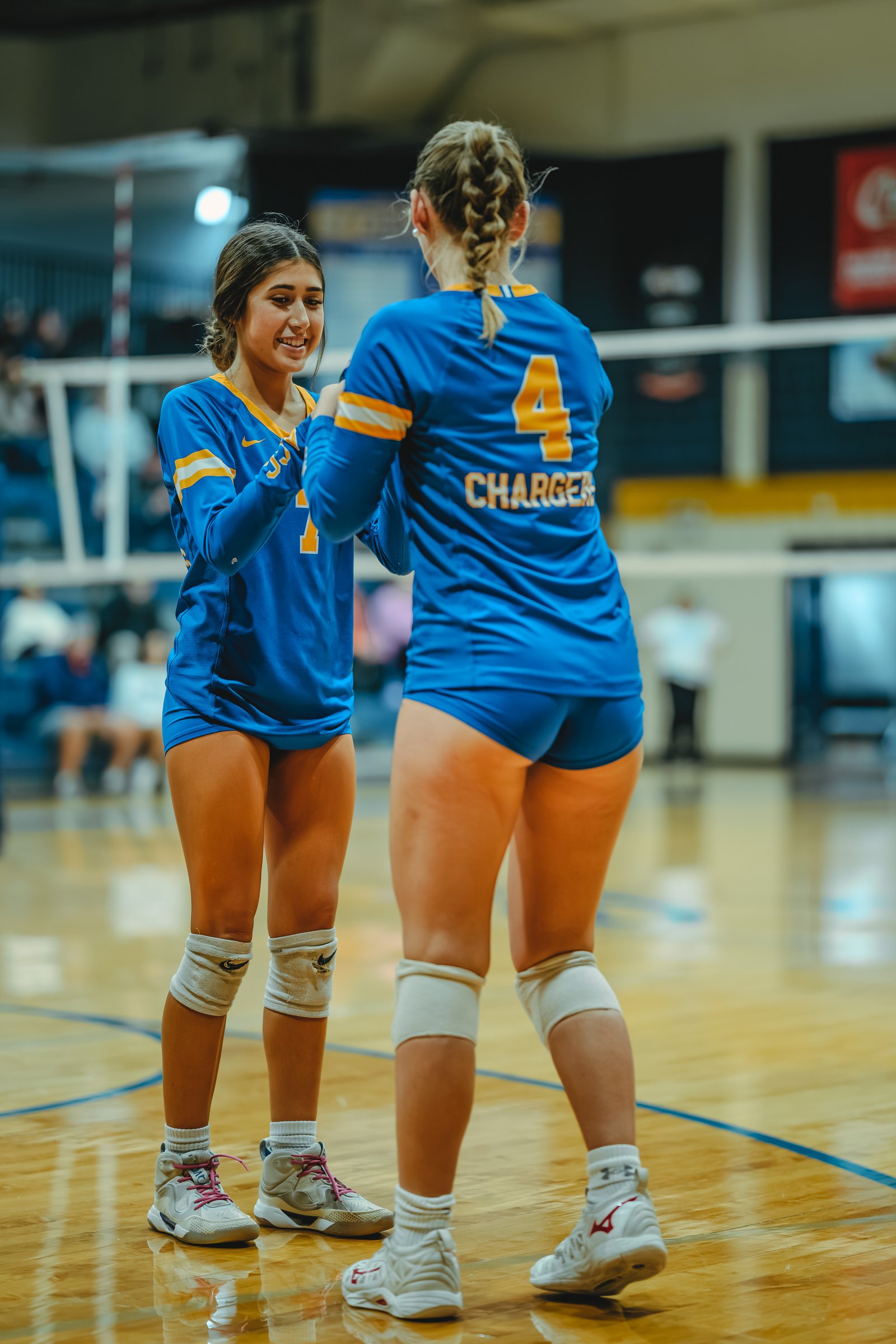 A player in blue with jersey number 7 high-fives a player in blue with jersey number 4 and the name CHARGER on the court.