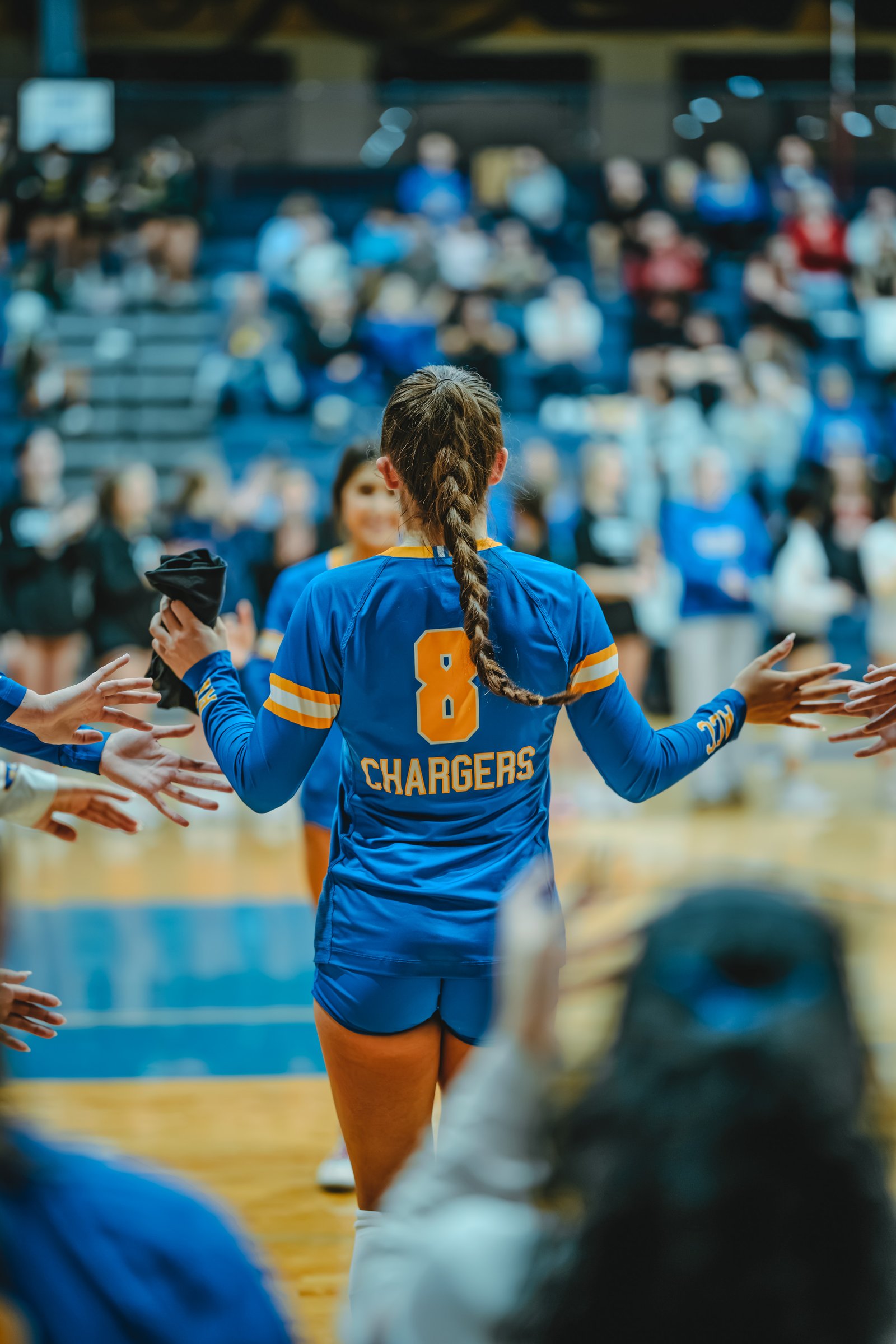 A player in blue with number 8 and "CHARGERS" on her jersey high-fives teammates on the court.