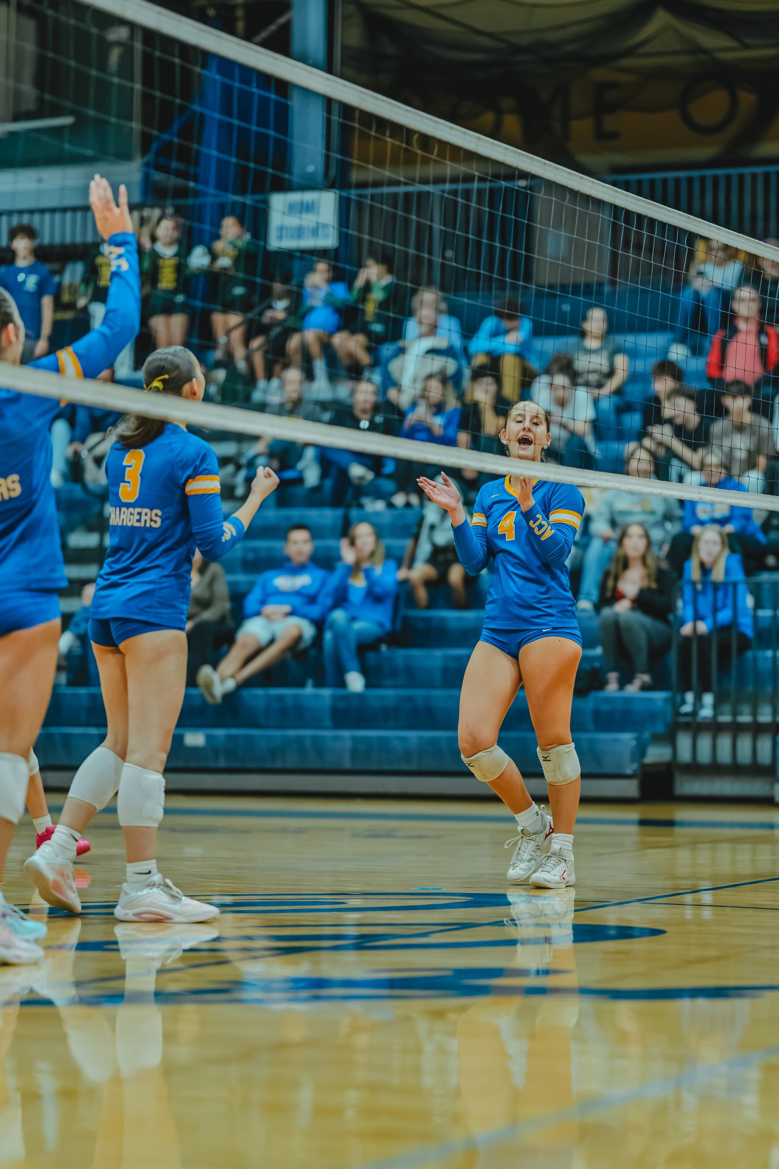 A player in blue with jersey number 4 celebrates, while a player in blue with jersey number 3 and the word CHARGERS on her back reacts on the court.