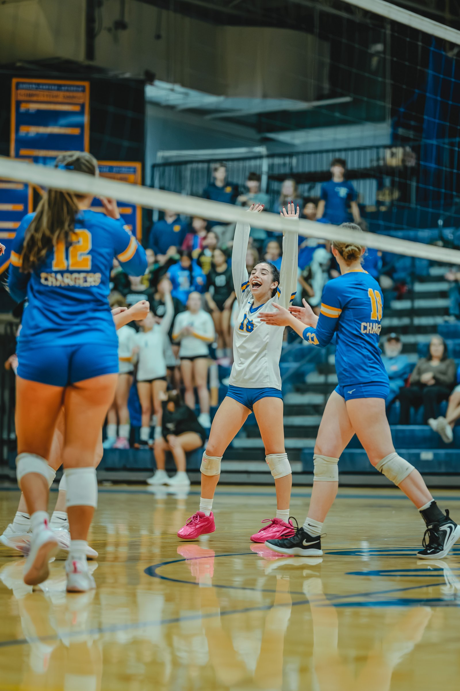 A player in white with number 16 celebrates with teammates in blue jerseys, one with number 12 and another with number 33, during a volleyball game.