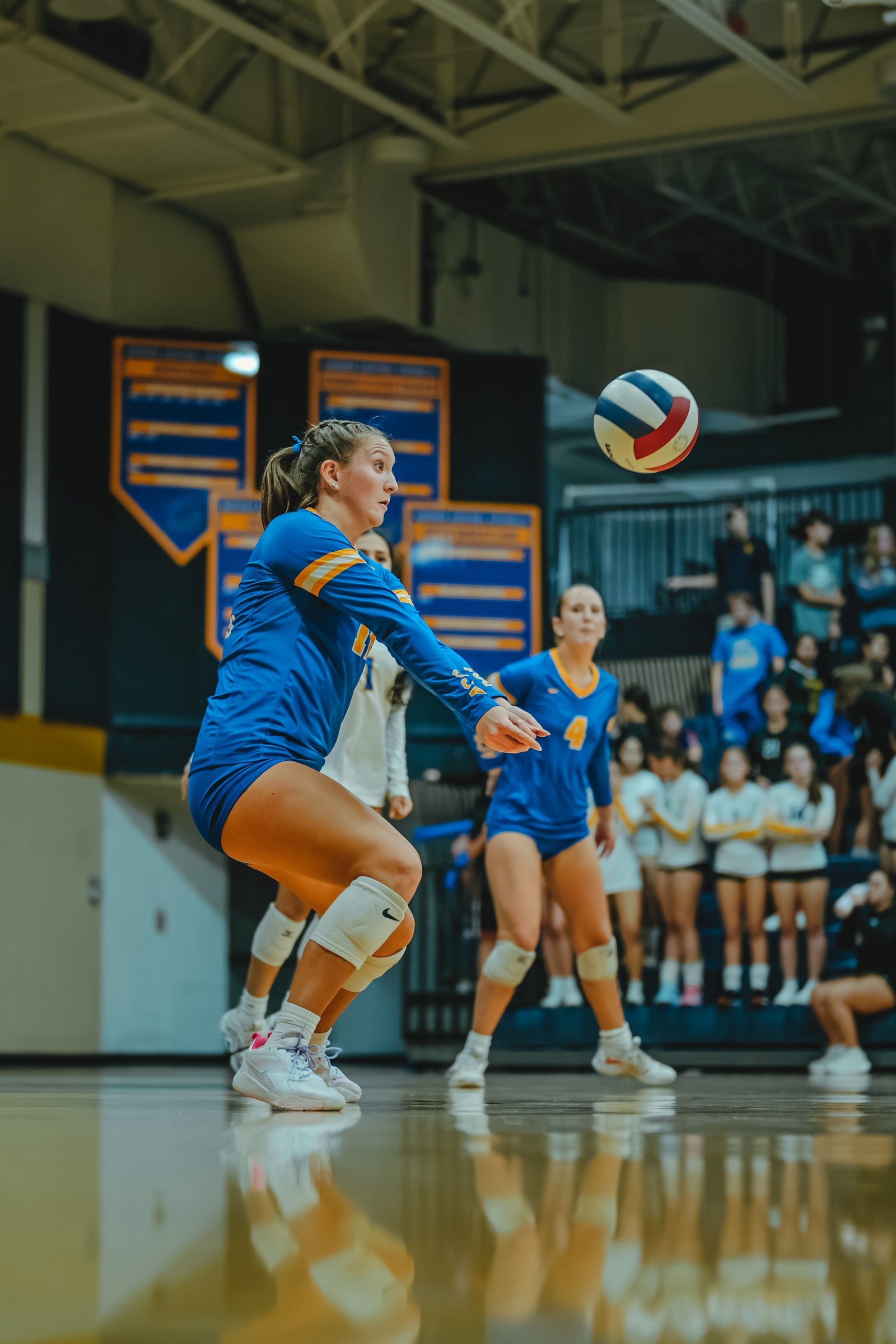 A player in blue with yellow trim prepares to pass the ball. A player in blue with number 4 and a player in white are on court.