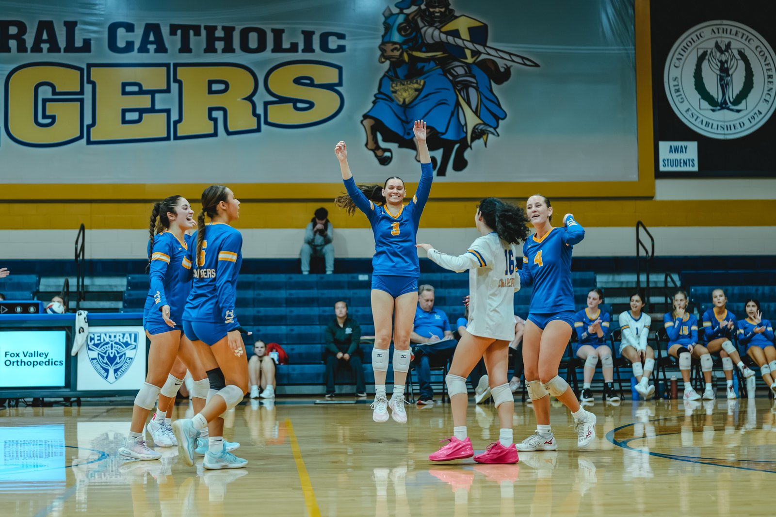 Players in blue jump and celebrate, with player 3 in blue and player 4 in blue visible, and player 16 in white on the court.