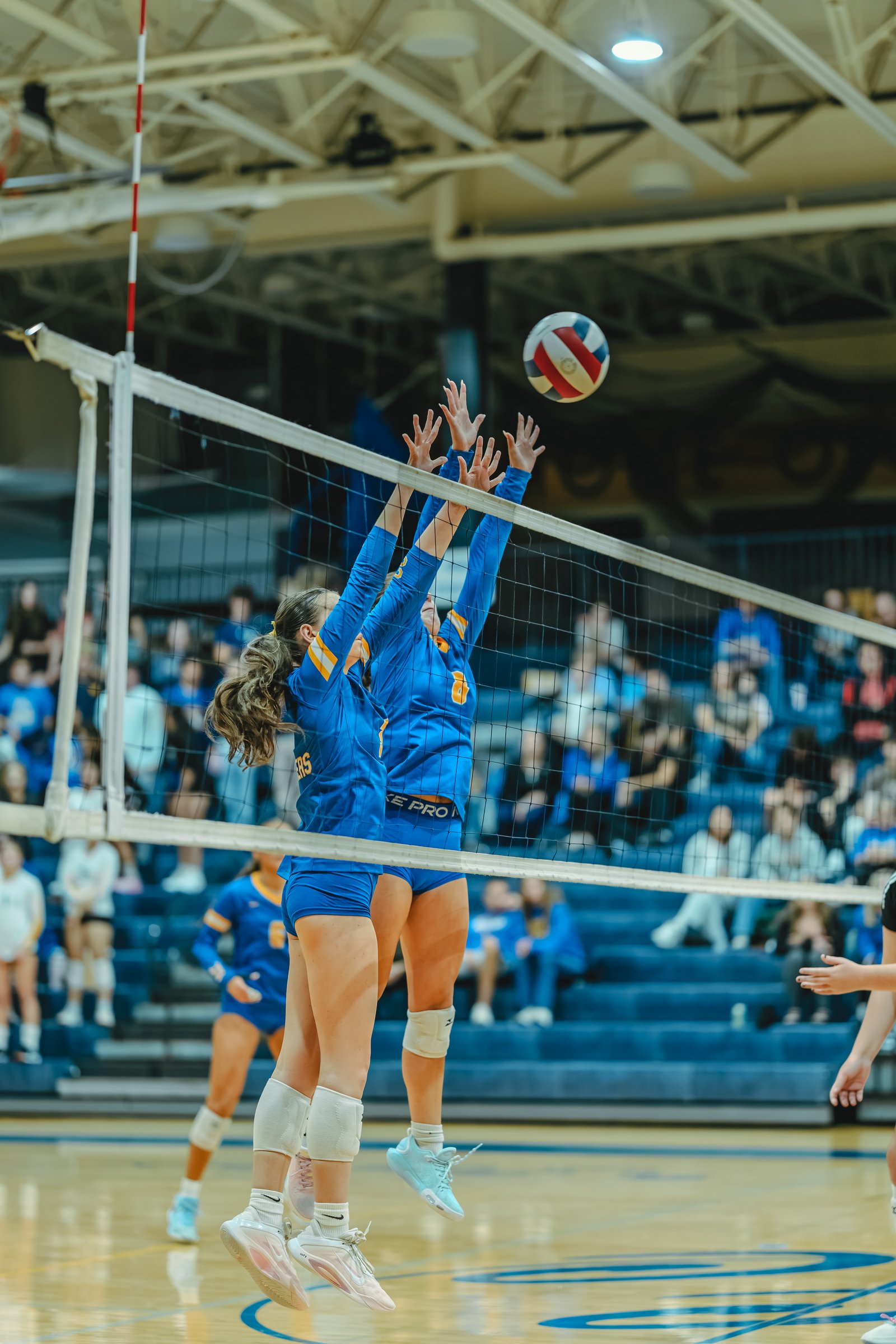 Players in blue jerseys jump to block a volleyball over the net. Player 8 and player 1 are visible.