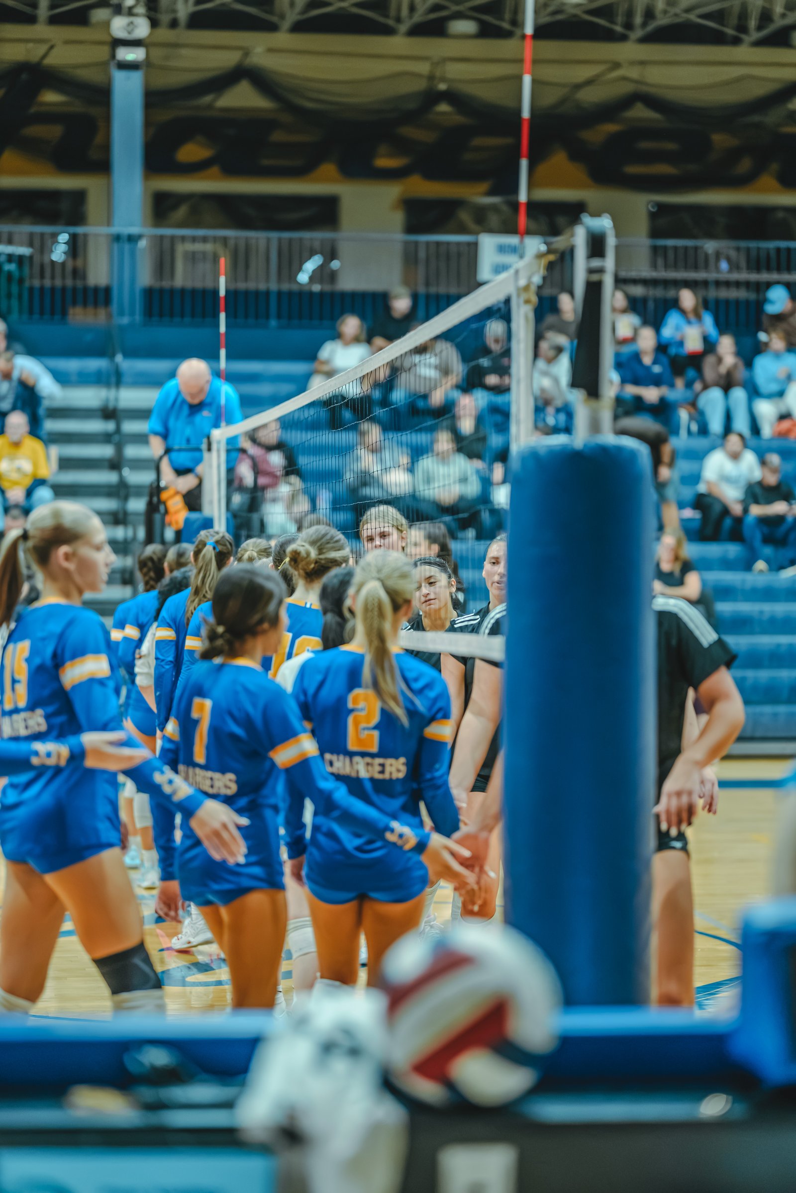 Players in blue and black jerseys huddle near the net. Player 15 in blue, player 7 in blue, and player 2 in blue are visible.