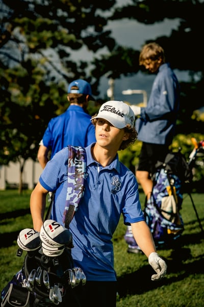 A player in blue carries a bag of clubs and looks to the side.