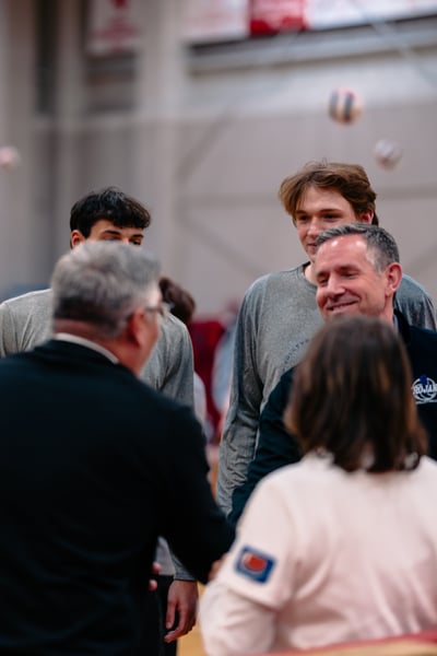 A player in a gray shirt smiles while shaking hands with a person in a black jacket.