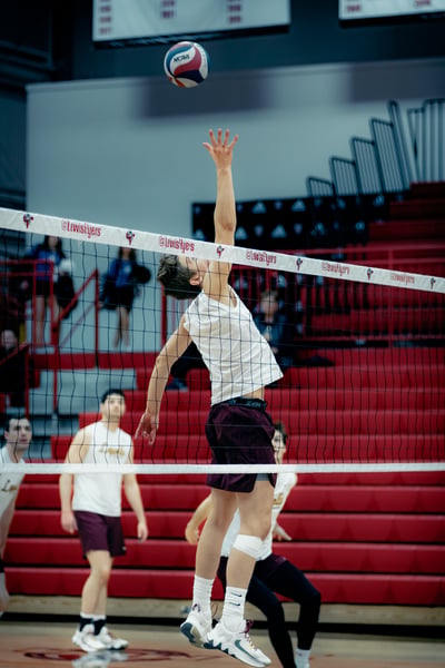 A player in white reaches overhead for the ball over the net.