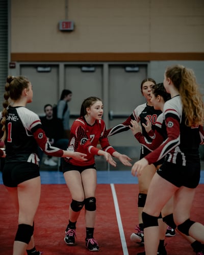 Players in red and black uniforms gesture with open hands on a red court.
