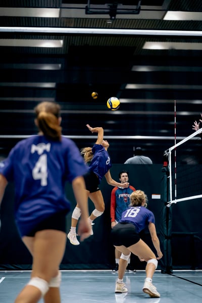 A player in blue jumps and reaches for the ball while another player in blue crouches low.