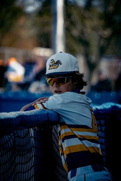 A player in a white and gold striped shirt leans on a fence.
