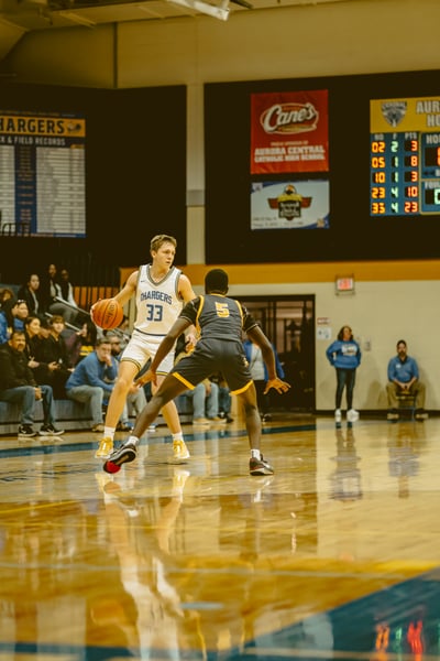 A player in white dribbles a basketball while a player in yellow and black guards him on a court.