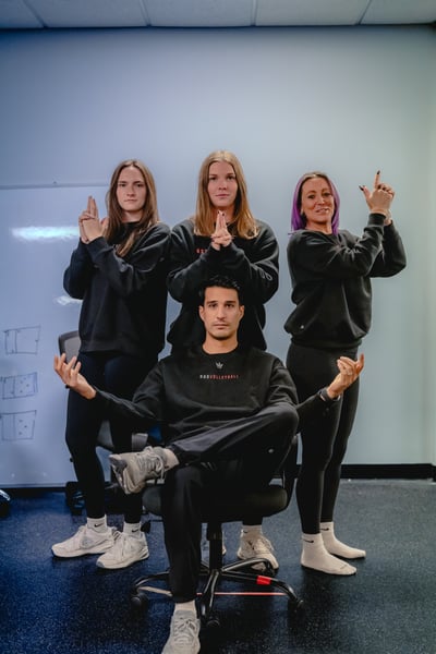 Four people in black tops pose with raised hands around a chair.