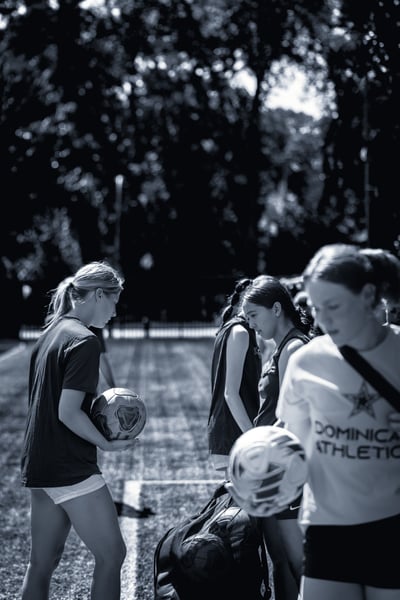 A player in a dark shirt holds a soccer ball while standing on a field.