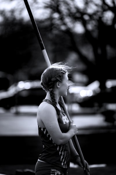 A person in a dark top holds a pole with both hands, looking to the side.