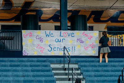 A player in a dark top and plaid skirt stands facing away from the camera, looking at a banner.