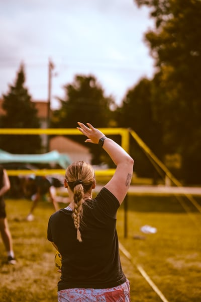 A player in black extends their right arm overhead while holding a yellow ball.