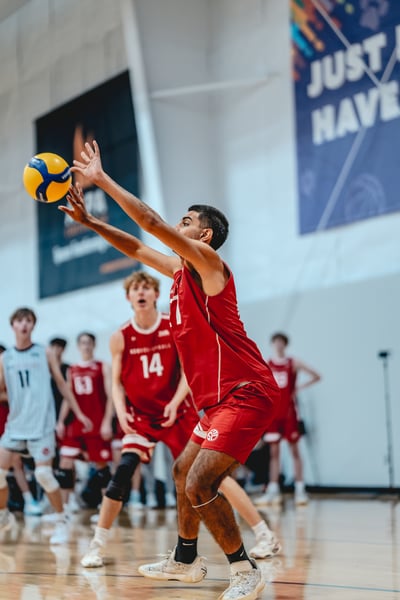 A player in red reaches overhead for the ball while other players in red and white stand ready.