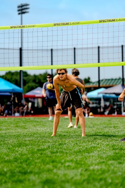 A player in black shorts with blue trim bends over on the grass court, with other players and tents in the background.