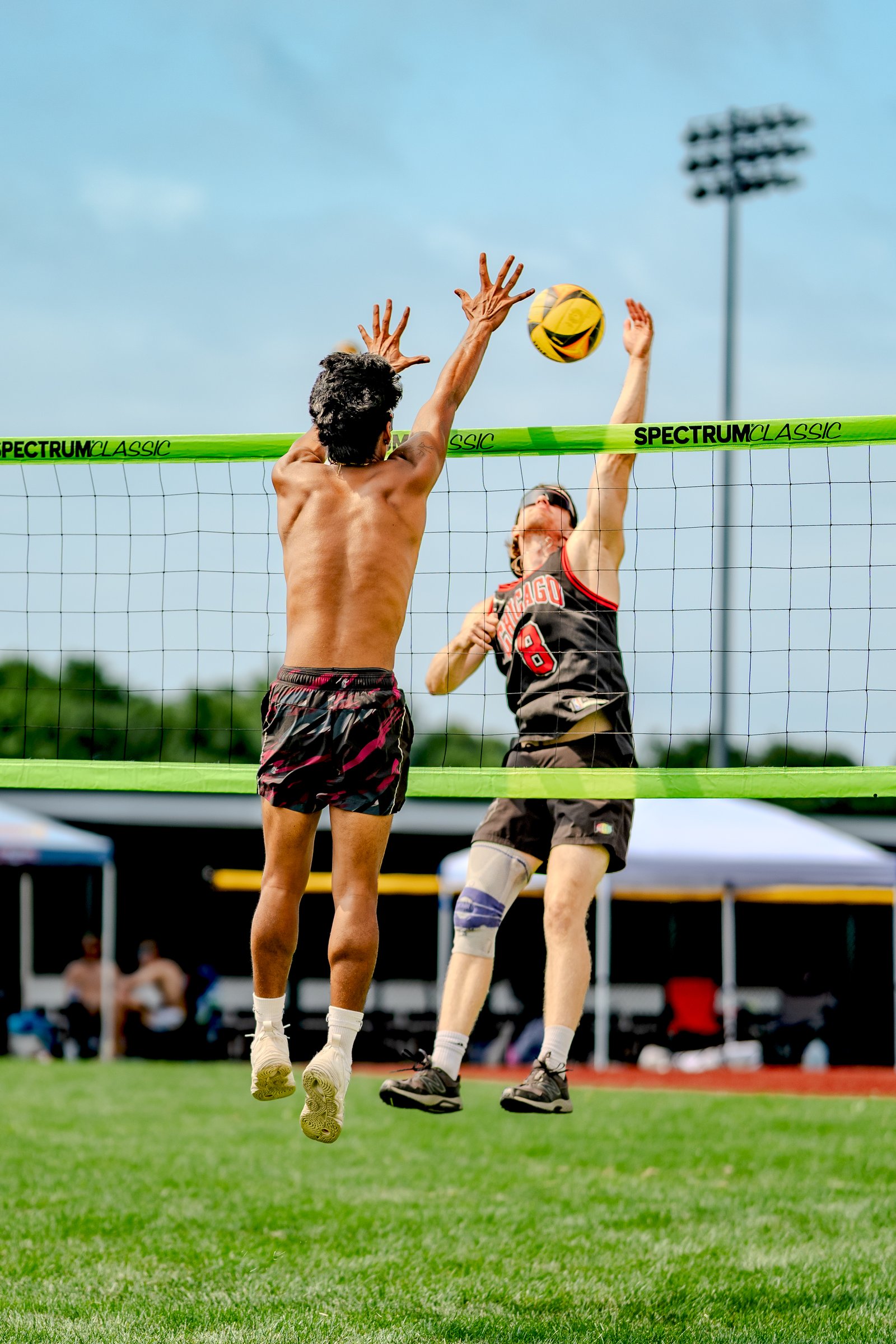 Two players jump at the net, one in black with red trim and number 8, the other shirtless, reaching for the ball.