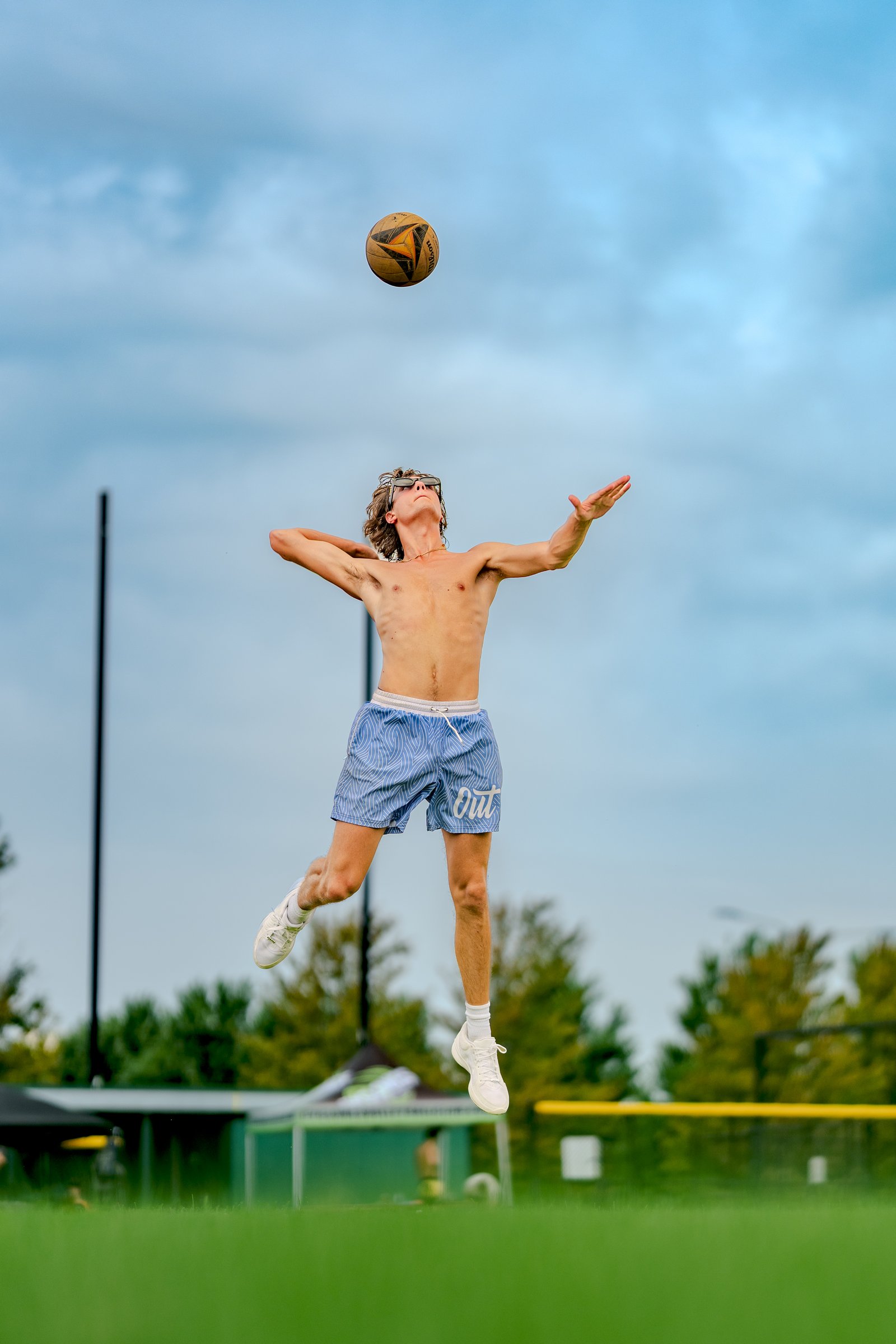 A player in blue shorts jumps to hit a volleyball against a cloudy sky.