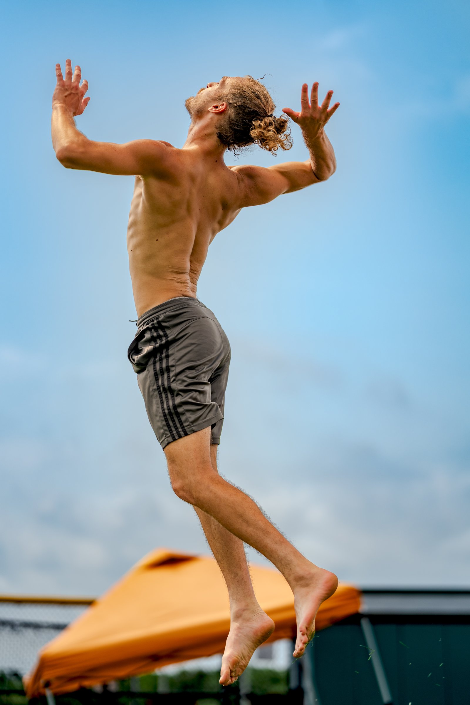 A player in gray shorts jumps with arms raised against a blue sky.
