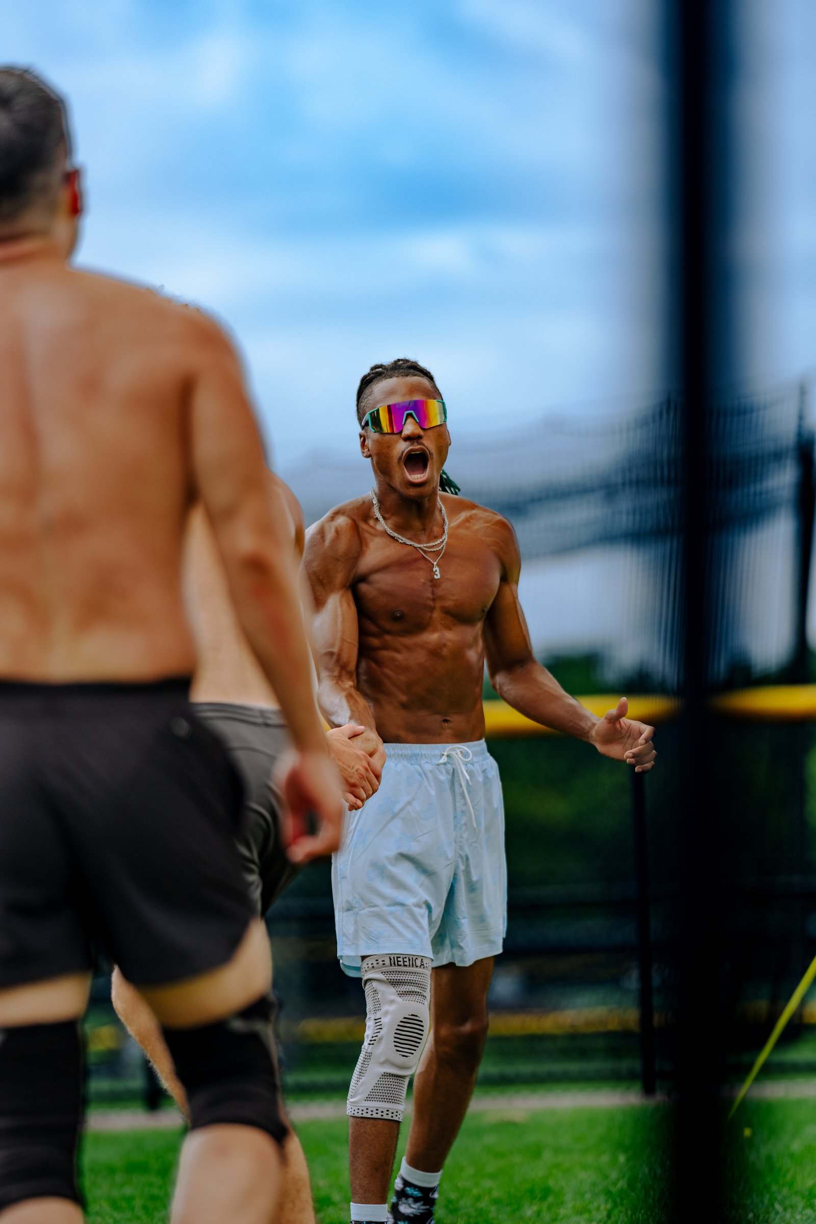 A player in light blue shorts and a player in black shorts are on the court, with a player in the foreground yelling.