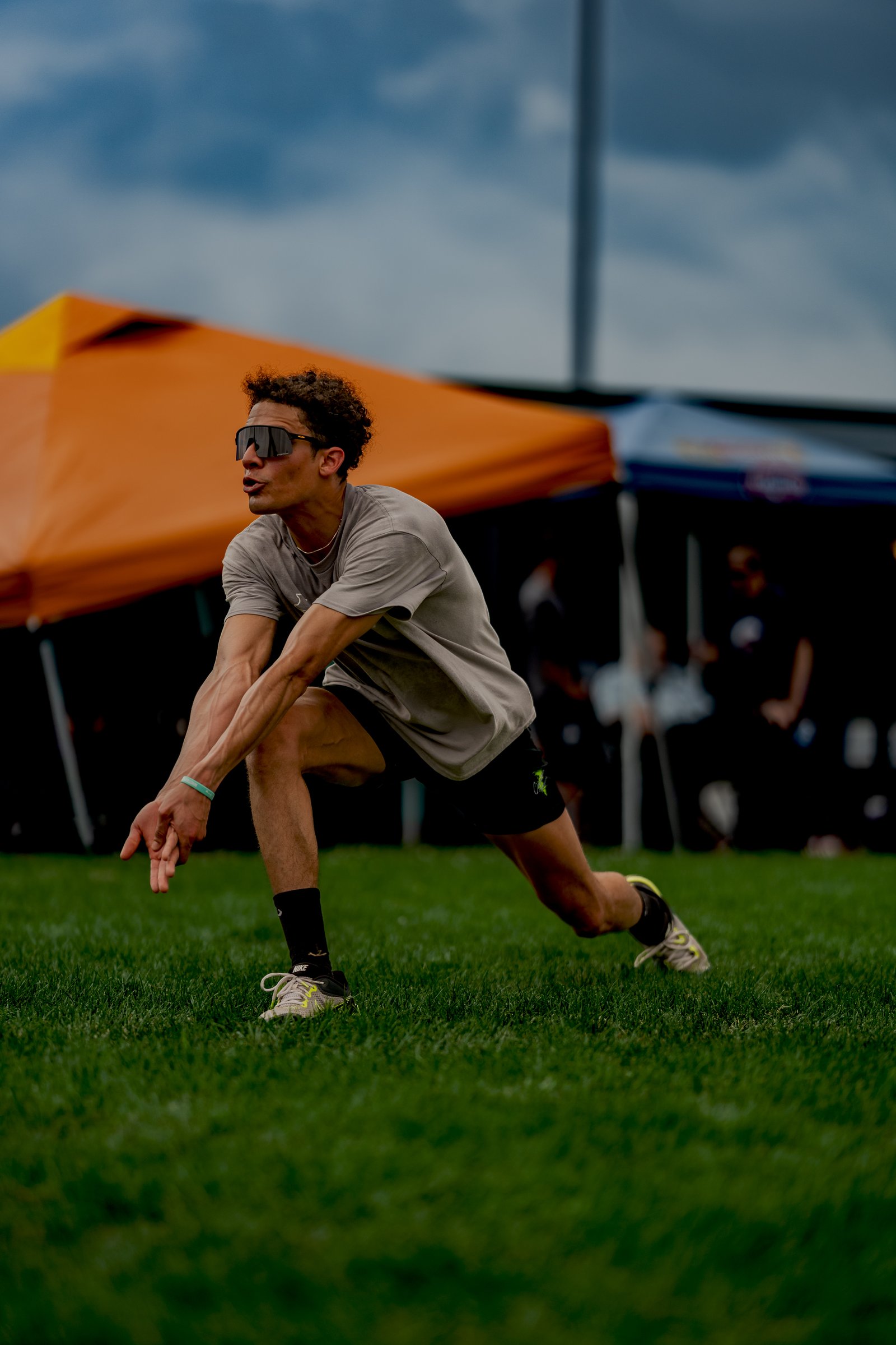 A player in a gray shirt and black shorts dives for the ball on the grass with tents in the background.