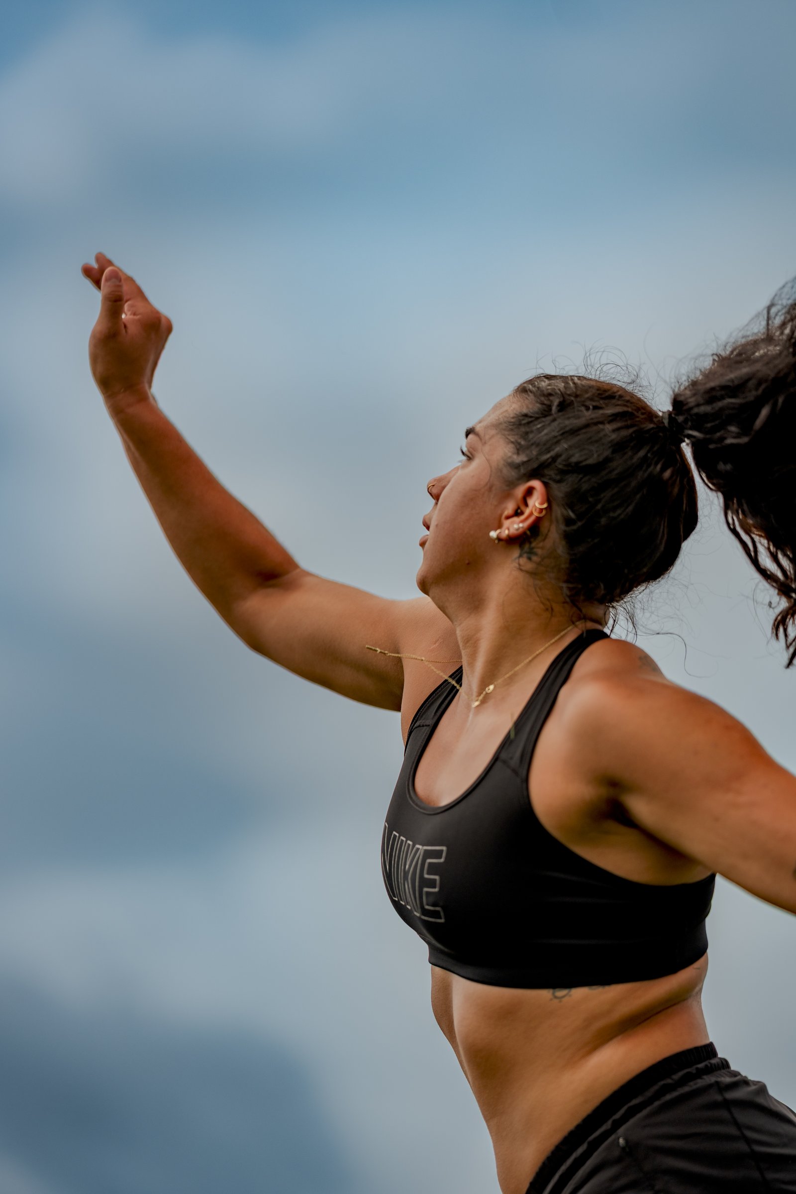 A player in a black top with a Nike logo reaches up against a cloudy sky.