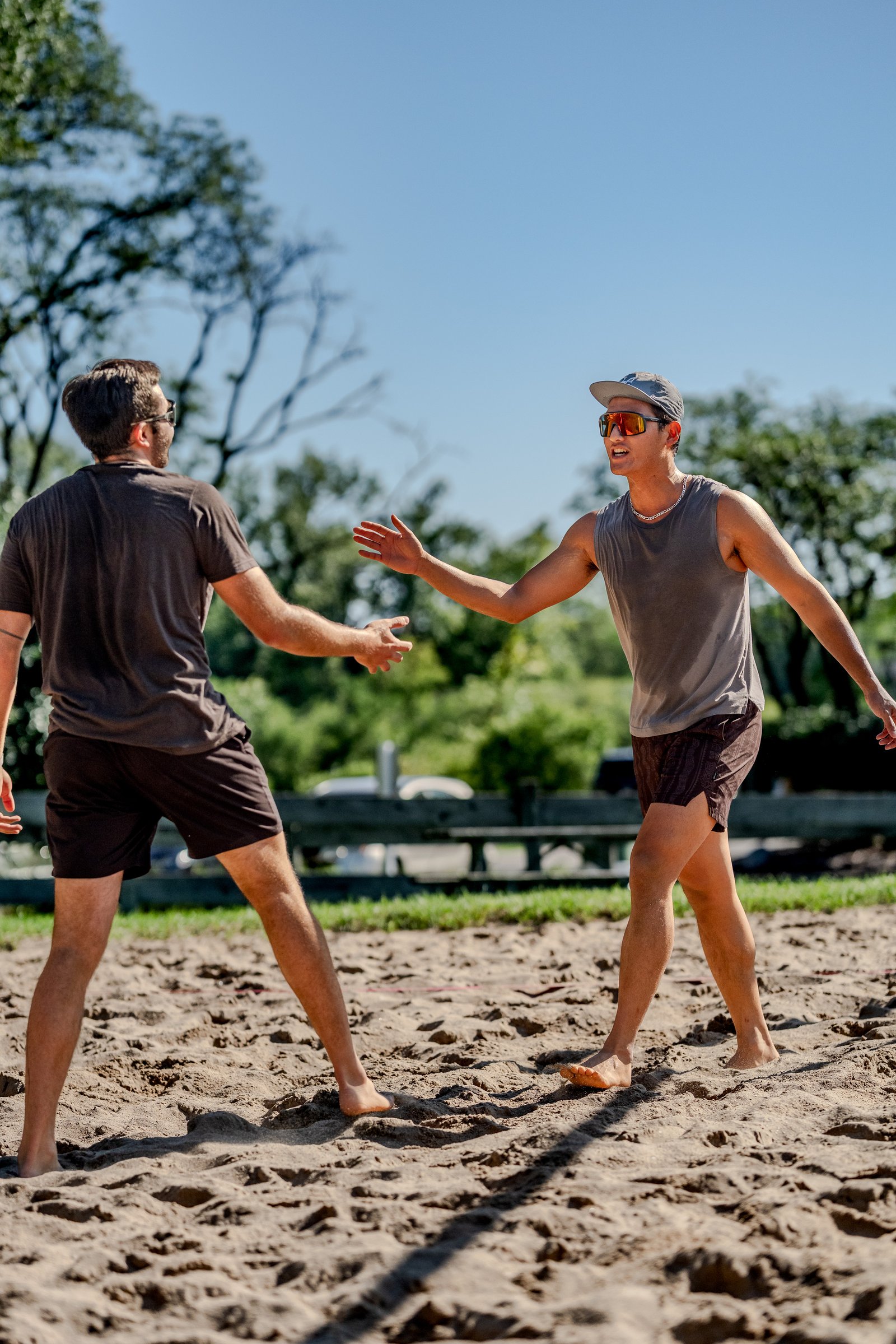 Two players in dark shorts and t-shirts reach out to each other on a sand court.