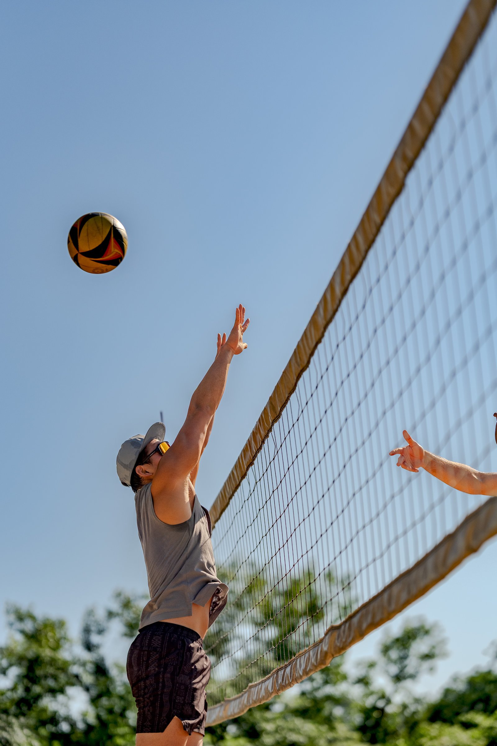 A player in a gray tank top and patterned shorts reaches for the ball during a volleyball game.