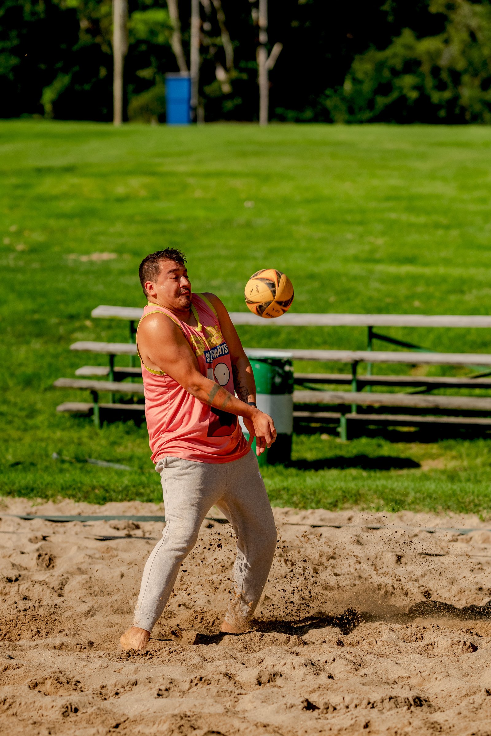 A player in a pink tank top with yellow trim attempts to hit a volleyball on a sand court.
