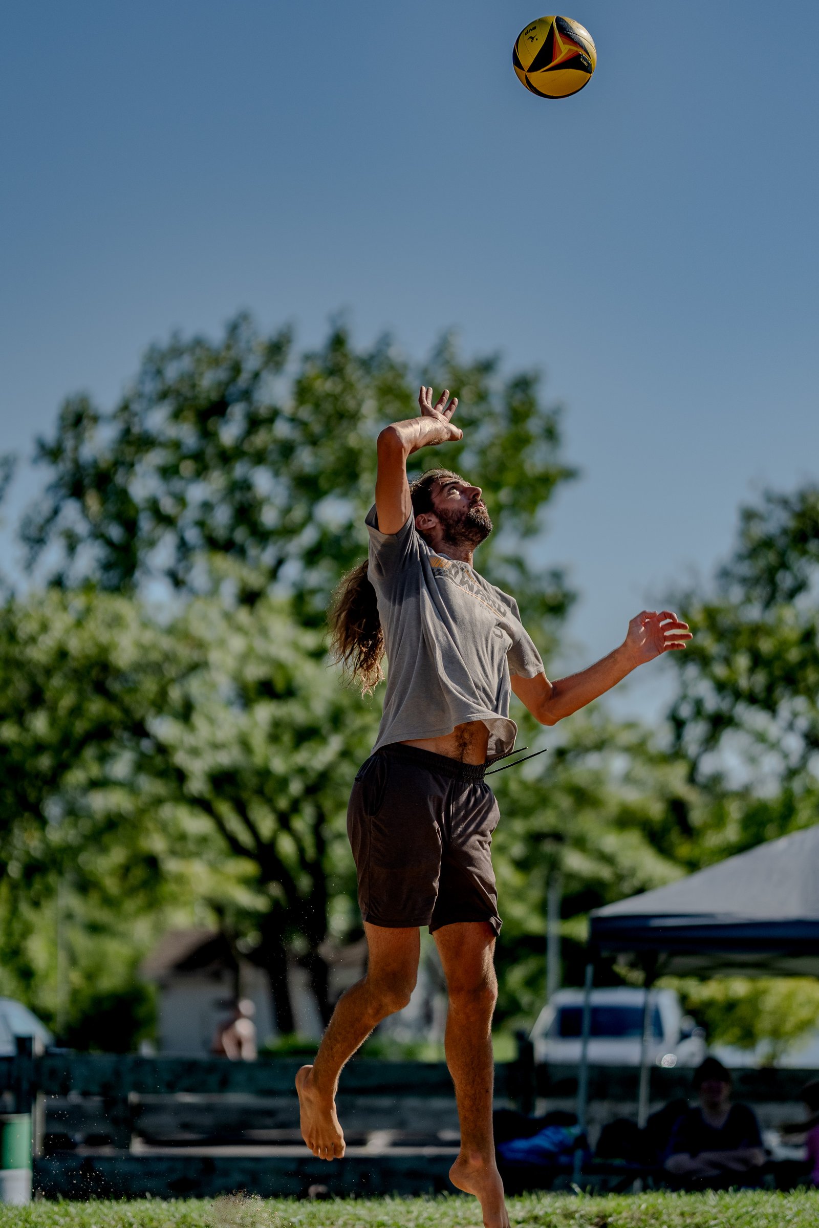 A player in a grey shirt and brown shorts serves a volleyball during a tournament.