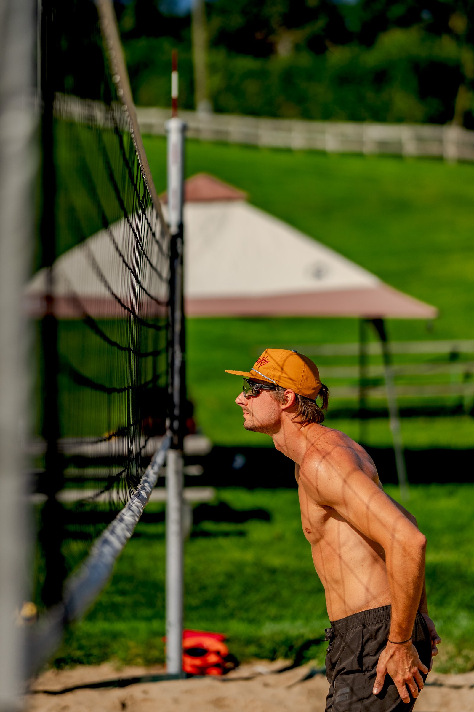 A player in black shorts and an orange cap watches the game near the net.