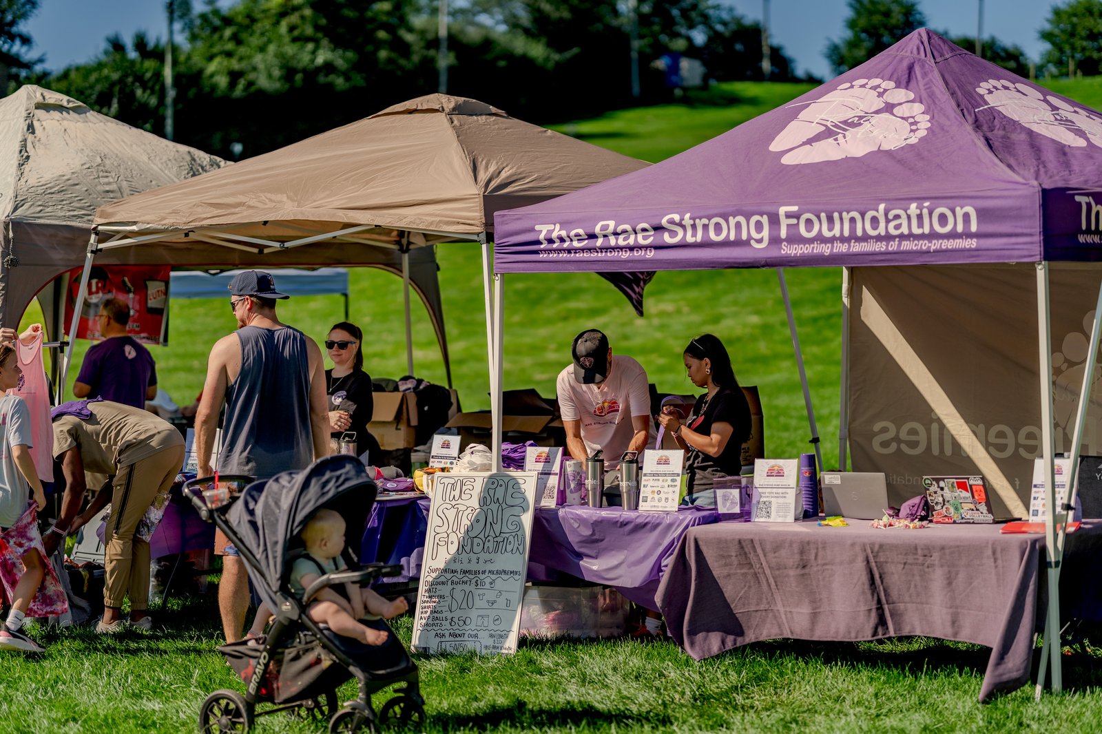 People gather at tents for the Rae Strong Foundation charity event, with a player in a pink top and a player in a black top visible.