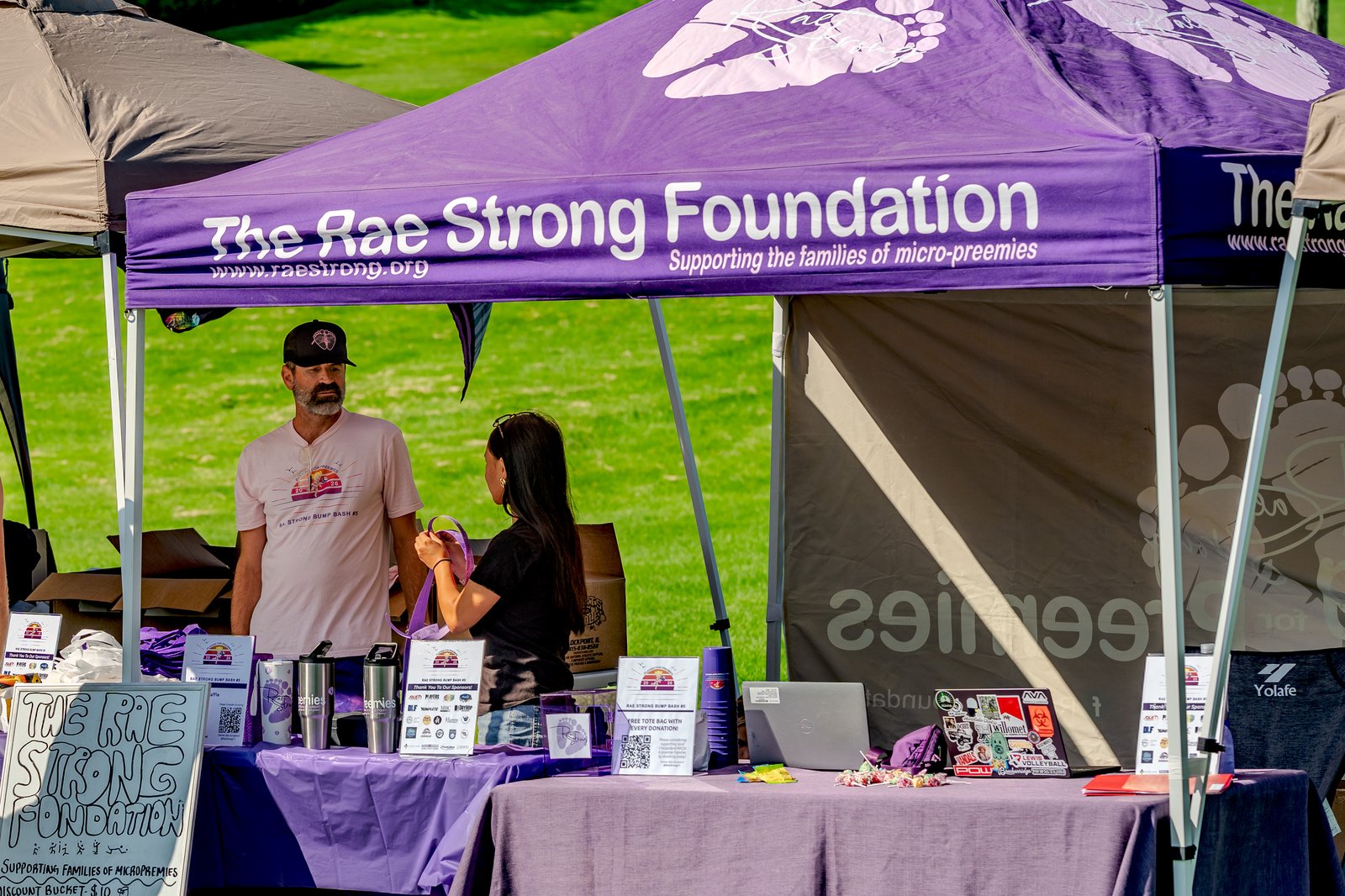 A man in a pink shirt and a woman in a black top stand near a tent at the Rae Strong Foundation event.