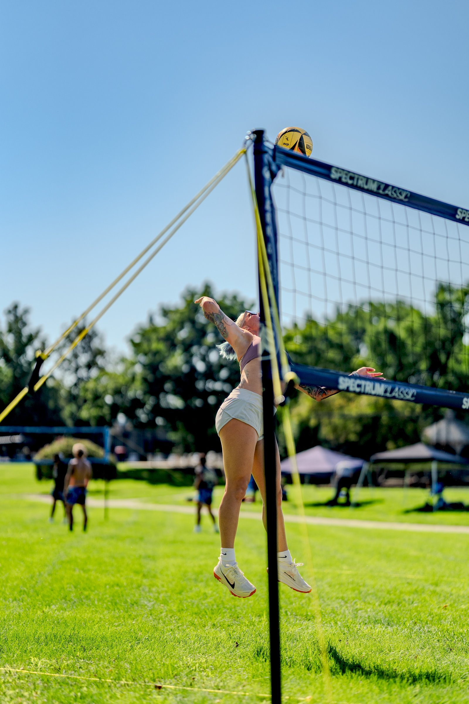 A player in a purple top and white shorts jumps to hit a volleyball over the net during a tournament.