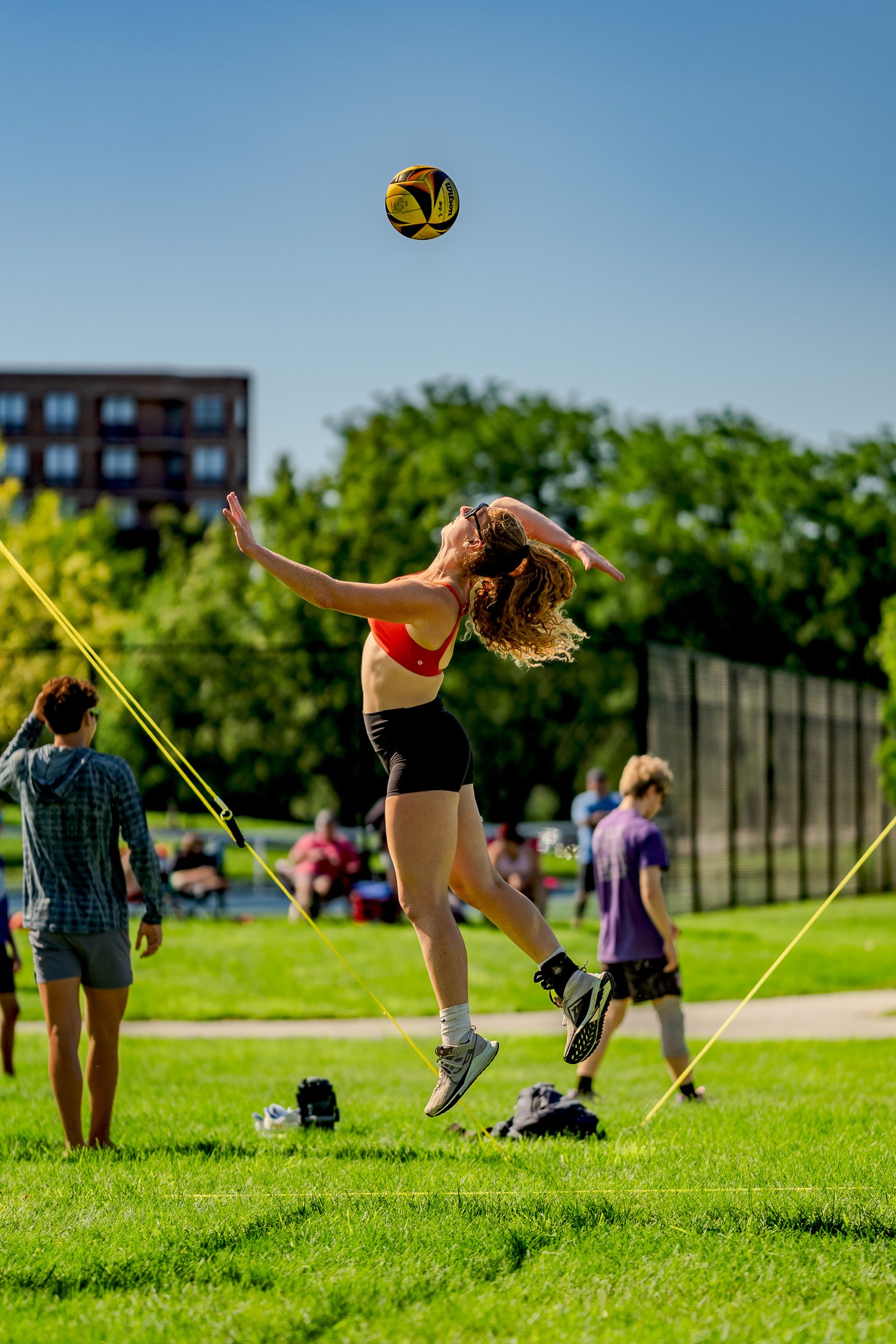 A player in a red top and black shorts jumps to hit a volleyball during a tournament on a sunny day.